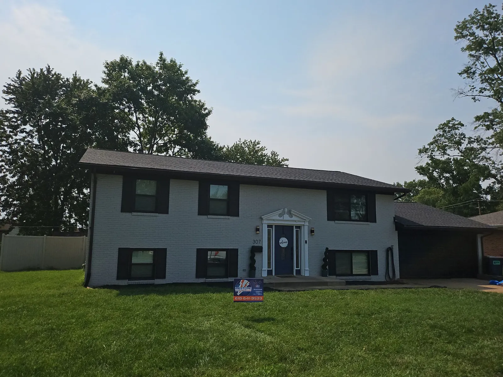 Completed dark architectural shingle roof on a white-painted brick split-level home with black shutters in Mascoutah, IL